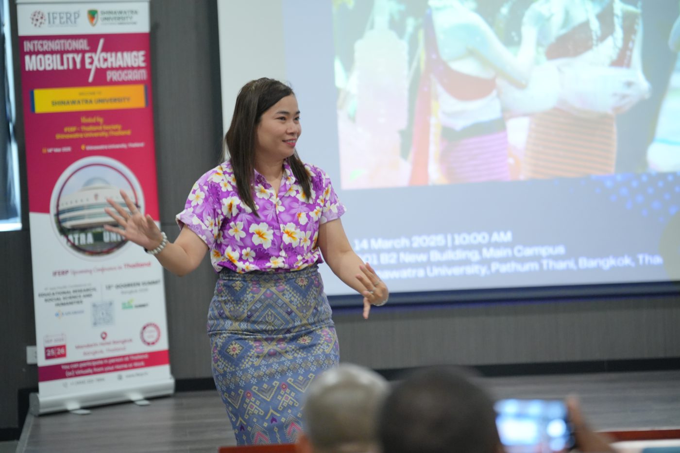 A presenter discussing her work beside a display board during a conference session